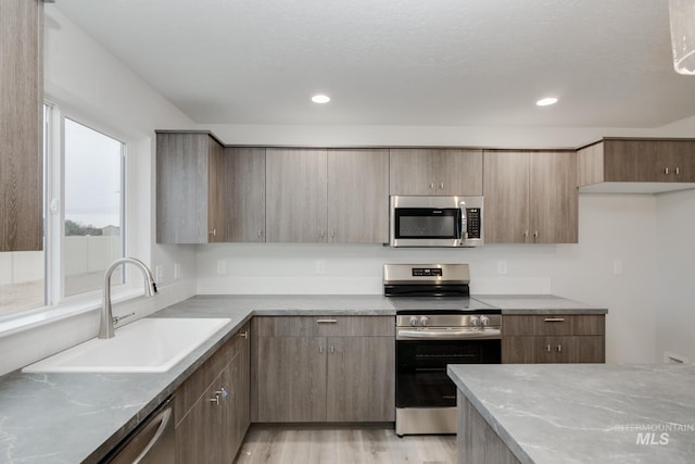 kitchen with sink, light stone counters, light hardwood / wood-style flooring, and appliances with stainless steel finishes