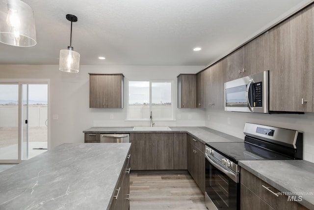 kitchen with sink, light hardwood / wood-style floors, decorative light fixtures, and stainless steel appliances