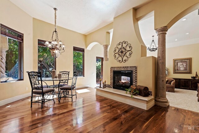 dining space featuring a chandelier, hardwood / wood-style flooring, a fireplace, arched walkways, and a high ceiling
