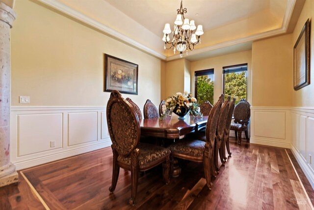 dining area featuring a chandelier, a decorative wall, a tray ceiling, wood finished floors, and a wainscoted wall