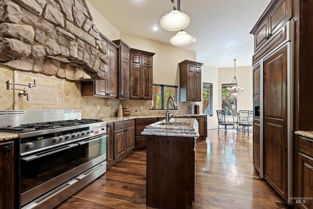 kitchen featuring high quality appliances, a center island with sink, decorative backsplash, dark wood-style floors, and dark brown cabinetry
