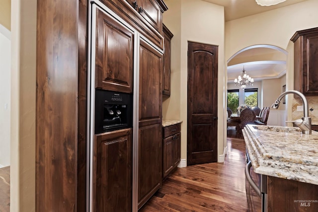 kitchen with dark wood finished floors, dark brown cabinetry, arched walkways, a chandelier, and a sink