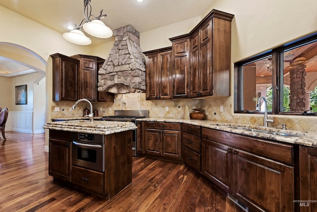 kitchen featuring a sink, appliances with stainless steel finishes, dark wood-style flooring, arched walkways, and dark brown cabinetry