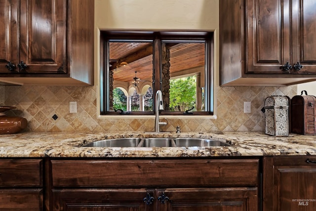 kitchen with a sink, dark brown cabinets, light stone counters, and decorative backsplash