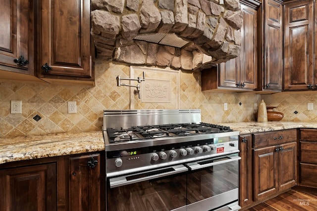 kitchen featuring high end stainless steel range, backsplash, light stone countertops, and dark brown cabinetry