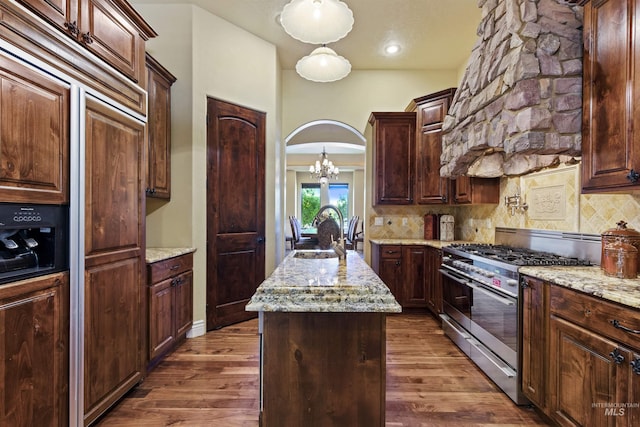 kitchen with high end range, a sink, a kitchen island with sink, backsplash, and a chandelier