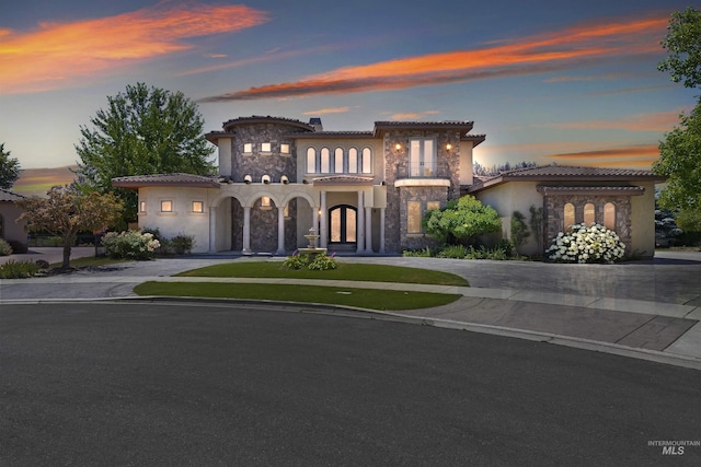 mediterranean / spanish-style house with stone siding, french doors, a tile roof, stucco siding, and curved driveway