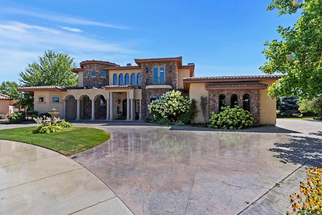 mediterranean / spanish-style house featuring stone siding, stucco siding, curved driveway, and a tile roof