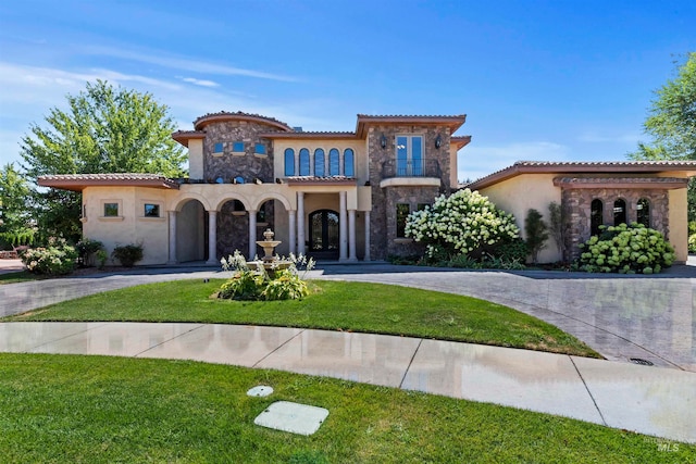 mediterranean / spanish-style house with stone siding, curved driveway, stucco siding, a tile roof, and a front lawn