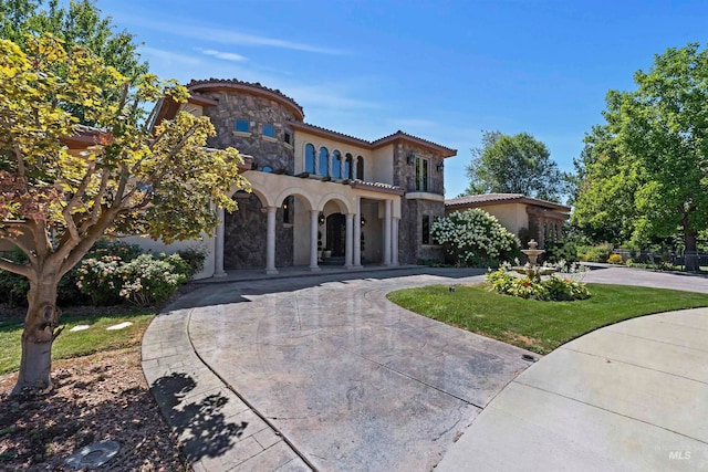 mediterranean / spanish house featuring a tiled roof, stucco siding, stone siding, and curved driveway