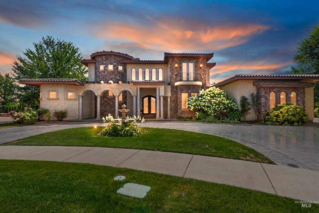 mediterranean / spanish home with stone siding, curved driveway, stucco siding, a tiled roof, and a balcony