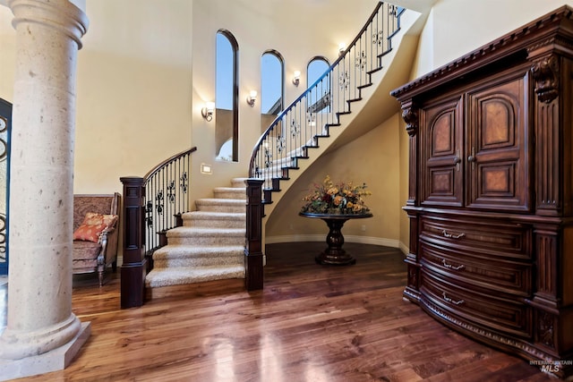staircase featuring ornate columns, a high ceiling, wood finished floors, and baseboards