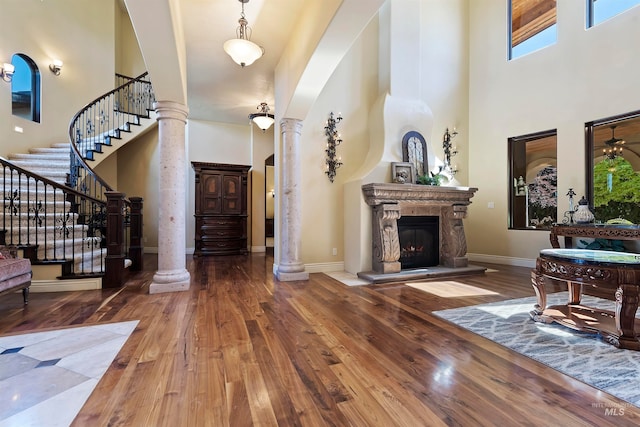 foyer entrance with decorative columns, a high ceiling, wood finished floors, baseboards, and a stone fireplace