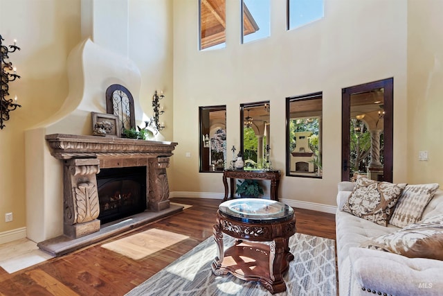 living room featuring healthy amount of natural light, a towering ceiling, wood finished floors, and baseboards