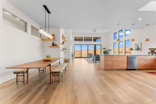 kitchen featuring light brown cabinetry, stainless steel dishwasher, light wood-type flooring, and pendant lighting