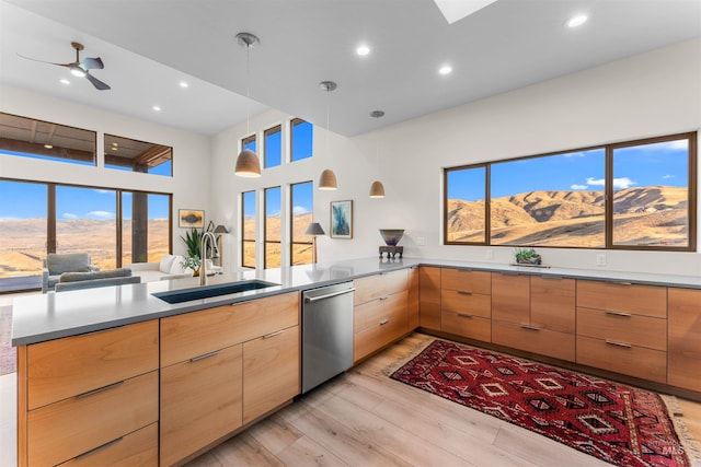 kitchen featuring pendant lighting, light wood finished floors, a sink, dishwasher, and a peninsula