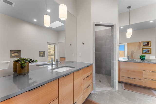 full bathroom with tiled shower, two vanities, a sink, and visible vents