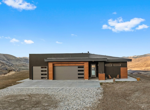 contemporary home featuring concrete driveway, an attached garage, a mountain view, and stucco siding