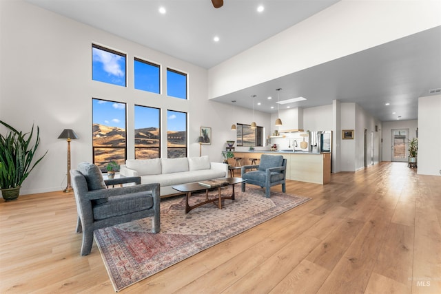 living room with light wood-style flooring, a high ceiling, ceiling fan, and recessed lighting