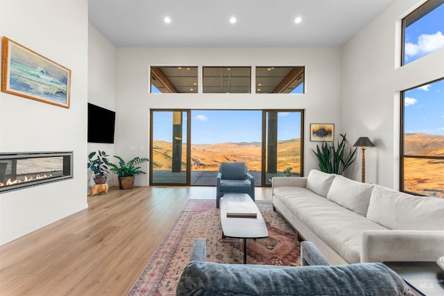 living room featuring a glass covered fireplace, recessed lighting, a high ceiling, and wood finished floors