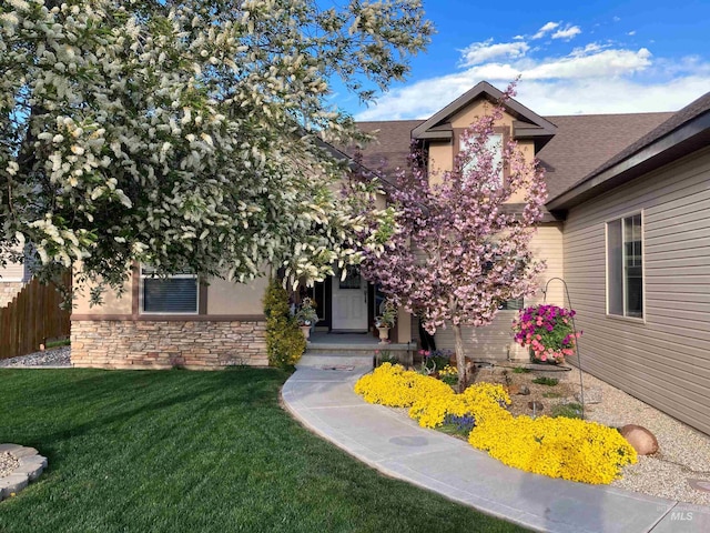 view of front of house featuring a shingled roof, fence, a front yard, stucco siding, and stone siding