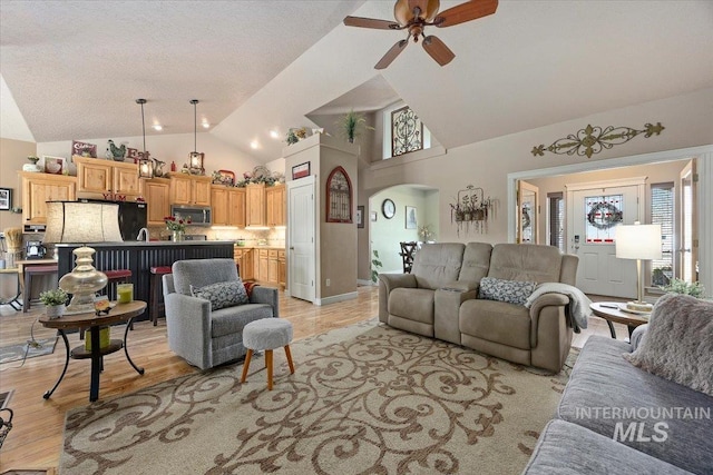 living area with arched walkways, a ceiling fan, light wood-type flooring, and a wealth of natural light