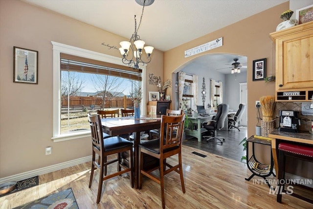 dining space with light wood-type flooring, arched walkways, baseboards, and ceiling fan with notable chandelier