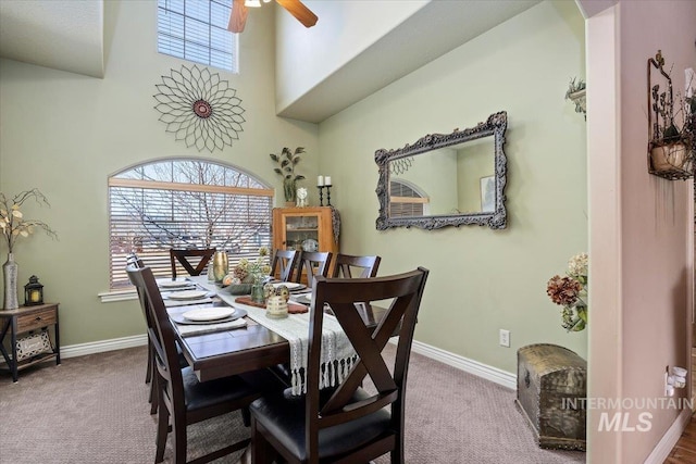 dining space with carpet flooring, baseboards, a towering ceiling, and ceiling fan