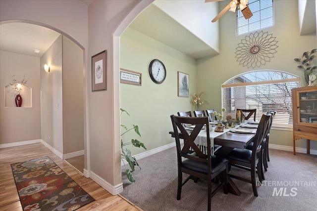 dining space with a ceiling fan, wood finished floors, arched walkways, and baseboards