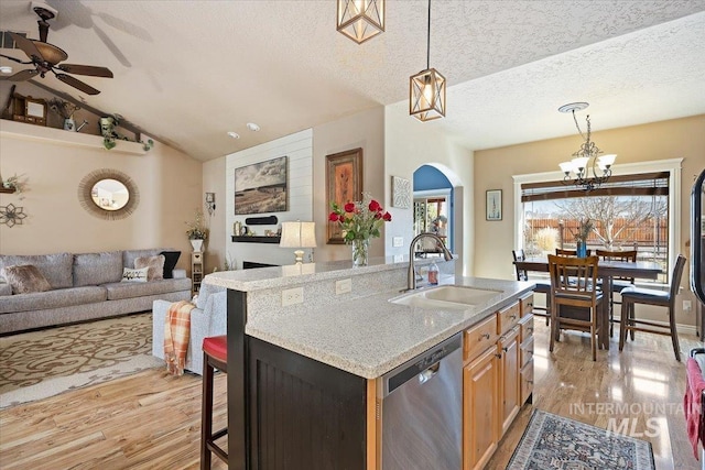 kitchen featuring vaulted ceiling, stainless steel dishwasher, light wood-style floors, a textured ceiling, and a sink