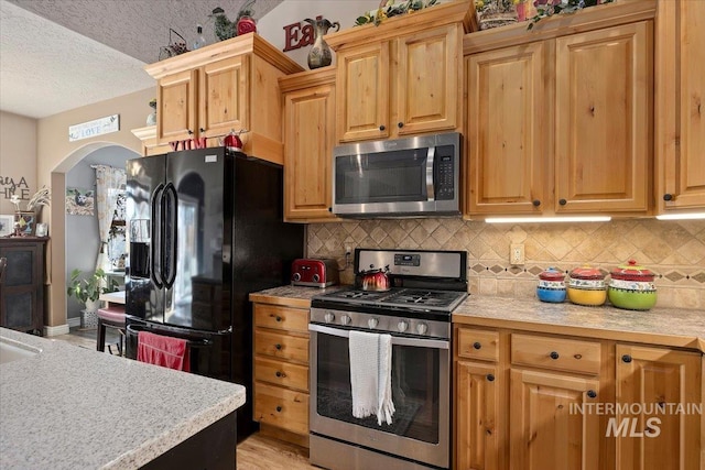 kitchen featuring light countertops, backsplash, arched walkways, and appliances with stainless steel finishes