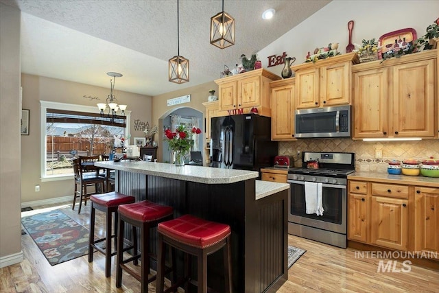 kitchen featuring backsplash, a kitchen island, light countertops, lofted ceiling, and stainless steel appliances