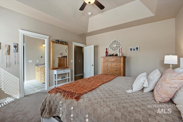 bedroom with carpet flooring, a raised ceiling, baseboards, and ensuite bathroom