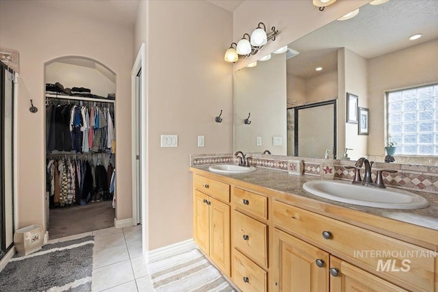 full bathroom with a walk in closet, tile patterned floors, a shower stall, and a sink