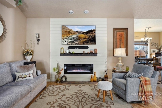 living room featuring a textured ceiling, wood finished floors, a large fireplace, baseboards, and a chandelier