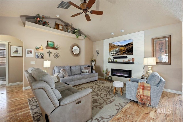 living room featuring wood finished floors, visible vents, a fireplace, arched walkways, and vaulted ceiling