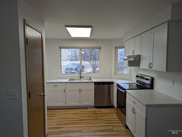 kitchen with light stone countertops, white cabinetry, sink, stainless steel appliances, and light wood-type flooring