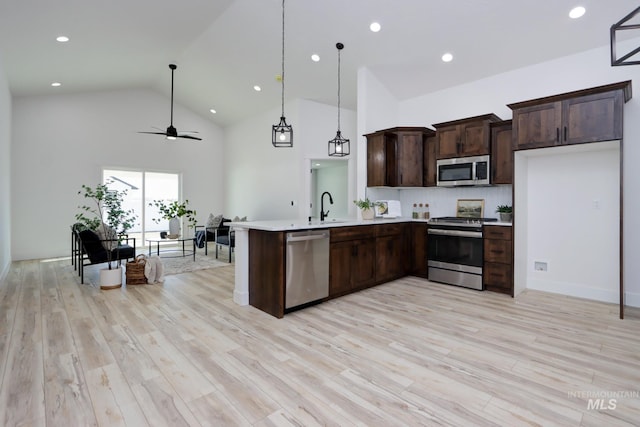 kitchen with sink, decorative light fixtures, light wood-type flooring, appliances with stainless steel finishes, and kitchen peninsula