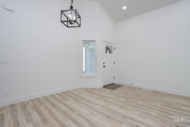 unfurnished room with a notable chandelier, a towering ceiling, and light hardwood / wood-style floors