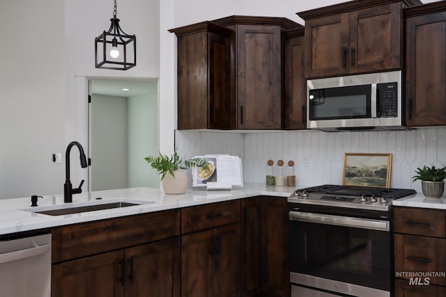 kitchen with sink, backsplash, stainless steel appliances, light stone countertops, and decorative light fixtures