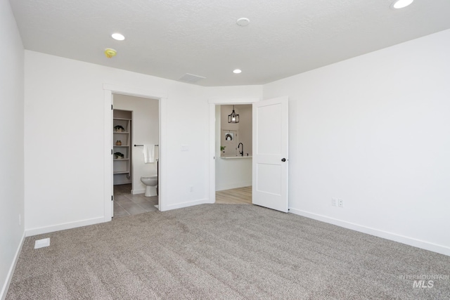 unfurnished bedroom with light colored carpet, ensuite bathroom, and a textured ceiling