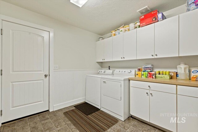 clothes washing area featuring a textured ceiling, wainscoting, cabinet space, and washing machine and dryer