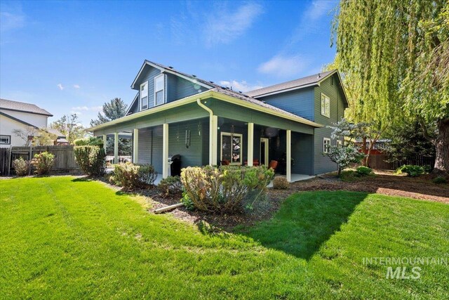 rear view of property featuring a lawn and fence