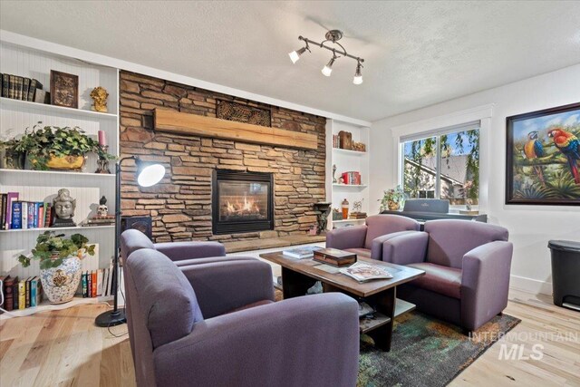 living room with a textured ceiling, built in shelves, wood finished floors, and a fireplace