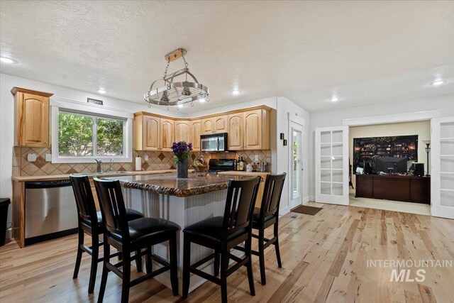 kitchen featuring appliances with stainless steel finishes, tasteful backsplash, a breakfast bar area, and light wood finished floors