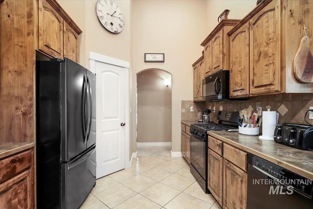 kitchen with a towering ceiling, light tile patterned floors, backsplash, and black appliances