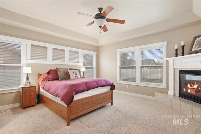 bedroom with a raised ceiling, a tile fireplace, ceiling fan, and light carpet