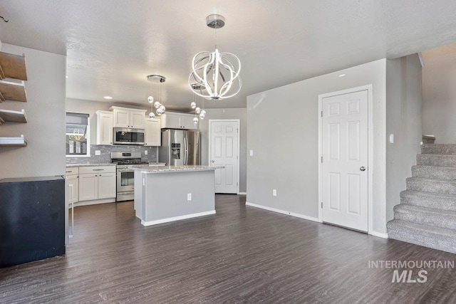 kitchen with appliances with stainless steel finishes, decorative light fixtures, an inviting chandelier, white cabinetry, and a kitchen island