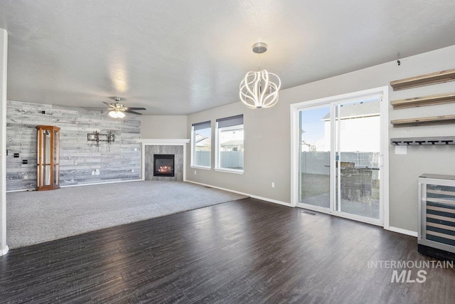 unfurnished living room featuring dark hardwood / wood-style flooring, ceiling fan with notable chandelier, wooden walls, a tile fireplace, and wine cooler