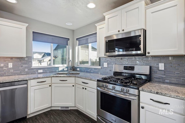 kitchen with light stone countertops, decorative backsplash, stainless steel appliances, sink, and white cabinetry